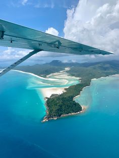 an airplane wing flying over a small island in the middle of blue water and white sand