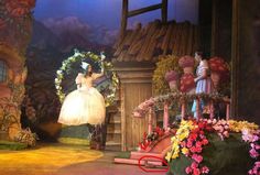 there is a woman in a white dress on the stage with flowers and wreaths around her