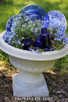 blue glass bottles and flowers in a white bowl on the ground with grass behind it