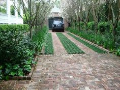 a car is parked in the middle of a brick driveway surrounded by trees and bushes