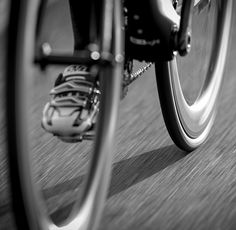 black and white photograph of a person riding a bike on the street with their foot in the air