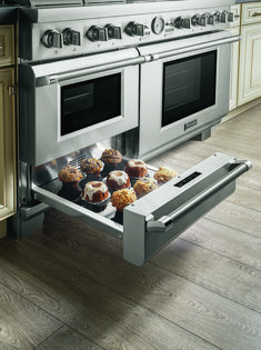 an open drawer in the middle of a kitchen with cupcakes and muffins