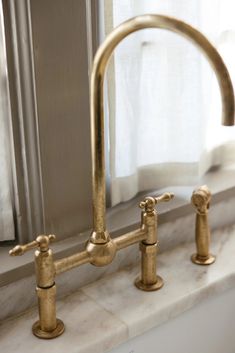 a gold faucet sitting on top of a white counter next to a window