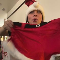 a woman in a santa hat holding up a red and white blanket with her mouth open