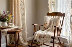 a rocking chair with a blanket on it next to a table and flowers in vases