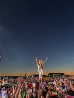 a woman standing on top of a crowd of people holding up their cell phones in the air