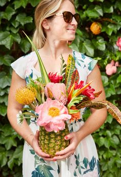 a woman holding a pineapple filled with flowers