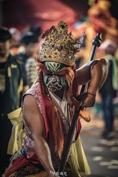 a man with a crown on his head is holding a stick and wearing a mask