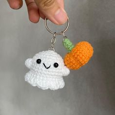 a hand holding a crocheted keychain with a white cloud and carrot on it