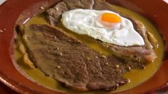 steak and eggs are served in a brown bowl on a white tablecloth with silverware