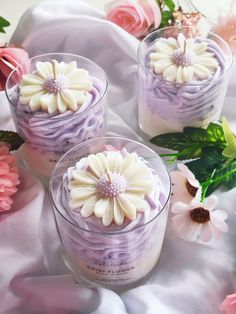 three small glass containers filled with purple and white frosted cake next to pink flowers