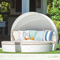 an outdoor daybed with pillows and drinks on it in the grass near some bushes