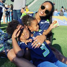 a woman and two children sitting on the ground at a football game with people in the background