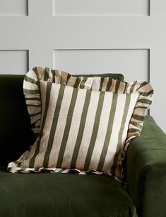 a green couch with two striped pillows on it's back and one in the middle