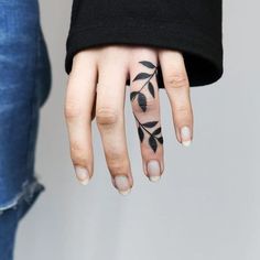 a woman's hand with black leaves on it and a white ring finger tattoo