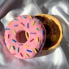 two donuts with pink frosting and sprinkles are on a white cloth