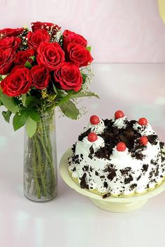 a vase filled with red roses next to a black forest cake on a white table