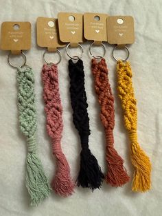 four different colored tassels are hanging on a white sheet with two tags attached to them