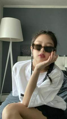 a woman sitting on top of a bed with her hand under her chin and wearing sunglasses