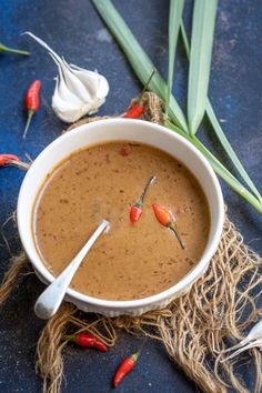 a white bowl filled with brown liquid next to garlic and red chili peppers on a blue surface