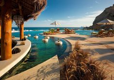 an outdoor swimming pool with lounge chairs and umbrellas next to the ocean on a sunny day