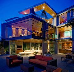 a large modern house with glass walls and lots of windows on the top floor is lit up at night