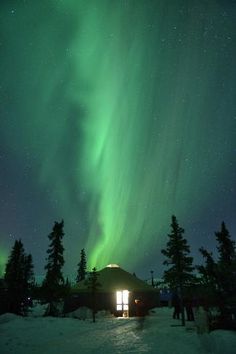 the aurora bore is lit up in the night sky above a cabin on snow covered ground