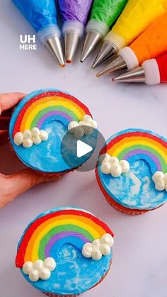 cupcakes decorated with rainbow icing and white frosting are being held by someone's hand