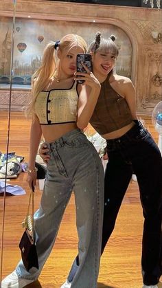 two young women standing next to each other in front of a mirror with their cell phones