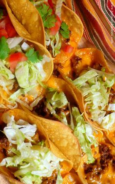 some tacos are sitting on top of a wooden tray with cheese and lettuce