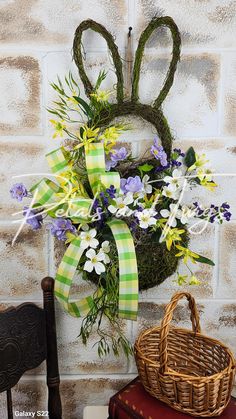 a basket with flowers and bunny ears on it sitting next to a wall mounted wreath