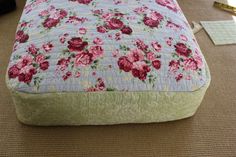 a bed with pink flowers on it sitting next to a lamp and other items in the room