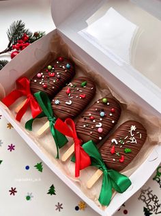 three chocolate covered cookies in a white box with green ribbon and bows on them, sitting next to christmas decorations