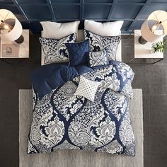 a bed with blue and white comforters in a room next to two lamps on the wall