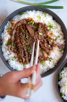 someone holding chopsticks in a bowl of rice with beef and onions on it