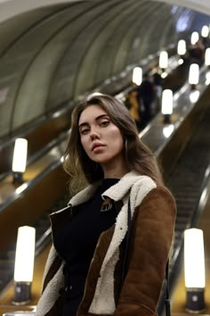 a woman standing on an escalator with her hand in her pocket and looking at the camera