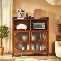 a wooden cabinet with glass doors in a living room next to a couch and potted plant