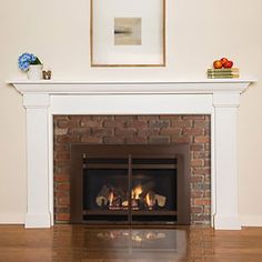 a fire place in a living room next to a painting on the wall and a vase with flowers