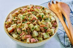 a bowl filled with potato salad next to a wooden spoon