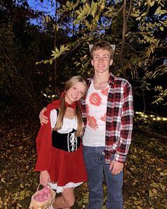 a young man and woman standing next to each other in front of trees at night