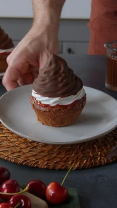 someone is decorating a cupcake with chocolate frosting and cherries on a plate