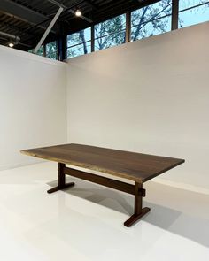 a wooden table sitting in front of a white wall with windows on the top floor