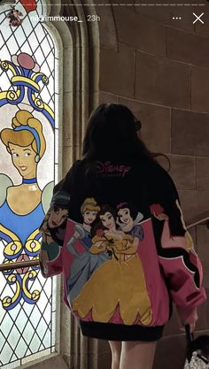 the back of a woman's jacket with disney characters on it, and a stained glass window behind her