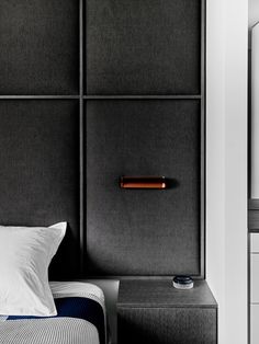 a bed with a black headboard and white pillows next to a wall mounted cabinet