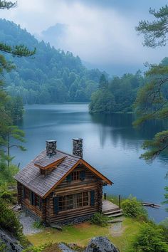 a cabin on the shore of a lake surrounded by trees and mountains with fog in the sky