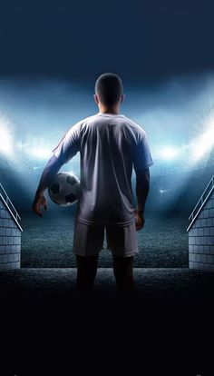 a man holding a soccer ball standing in front of a stadium full of people at night