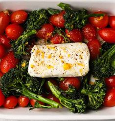 a white dish filled with tomatoes, broccoli and fish