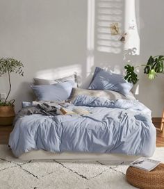 a bed with blue sheets and pillows in a room next to a potted plant