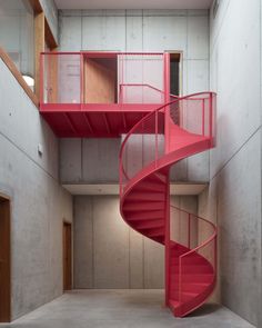 a red spiral staircase in the middle of an empty room with concrete walls and flooring