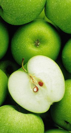 green apples are piled up with one apple sliced in half and the other whole on top